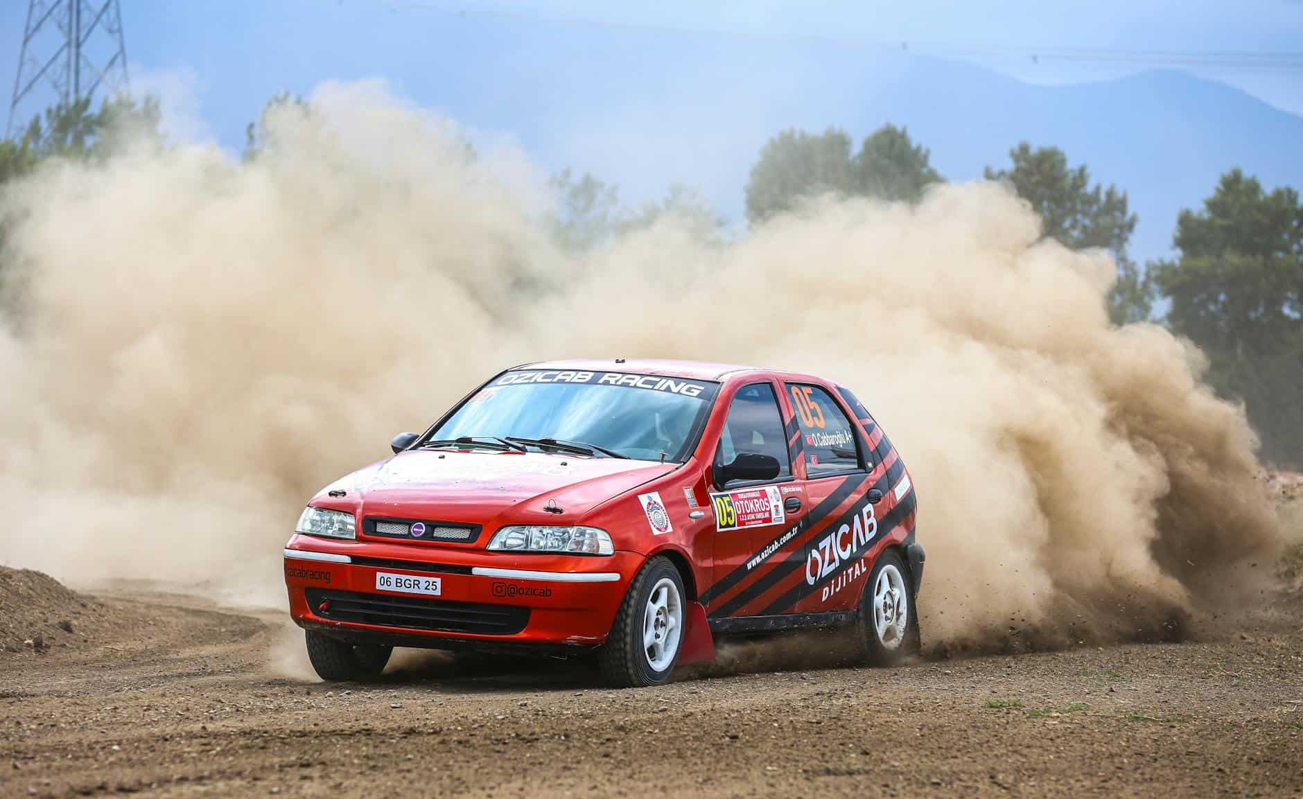 a red car driving through a dust cloud